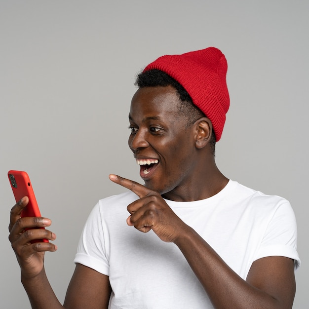 Un homme joyeux hipster africain porte un chapeau rouge discutant dans les médias sociaux, en riant