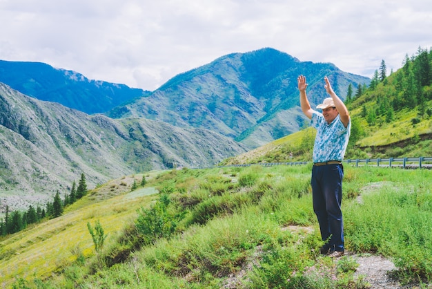 Homme joyeux près de l'autoroute parmi les montagnes géantes. Voyageur gai sur la colline parmi une végétation riche. Tourisme de montagne. Voyage en montagne.