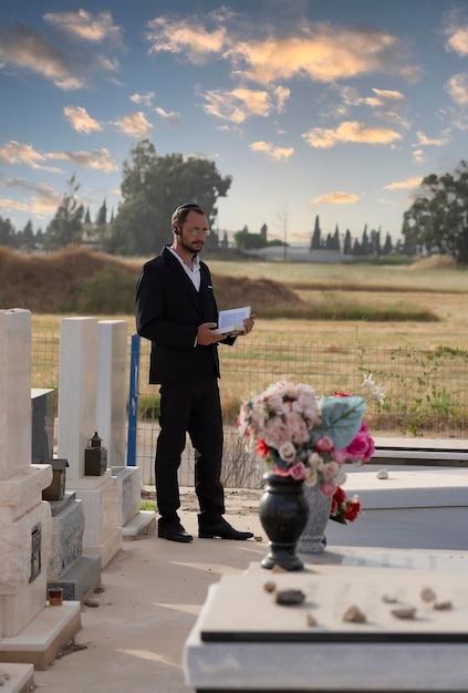 Photo homme juif barbu en kippa noire lisant une bible hébraïque priant prière dans un cimetière juif en israël mise au point sélective ancien cimetière juif dans la forêt juif hassidique tenant un livre torah rabbin