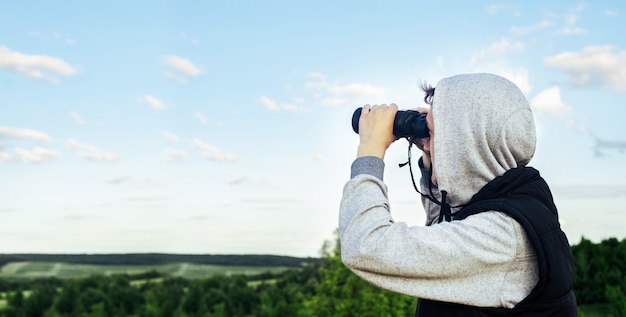 Un Homme Avec Des Jumelles Modernes Dans Le Ciel Et Des Collines Verdoyantes. Le Concept De Chasse, De Voyage Et De Loisirs De Plein Air.