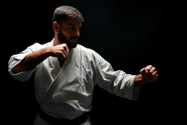 Homme de karaté dans un kimono en position de combat sur fond noir