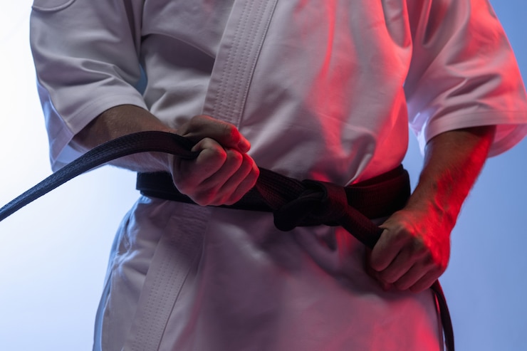 Photo homme en kimono blanc et ceinture noire karaté d'entraînement sur fond gris.