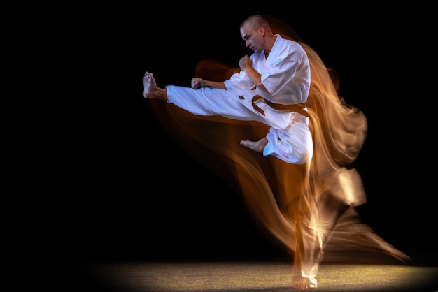 Homme en kimono blanc et ceinture noire karaté formation sur fond de studio noir.