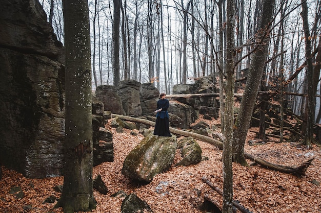 Homme en kimono noir pratiquant les arts martiaux avec une épée sur les rochers et fond de forêt