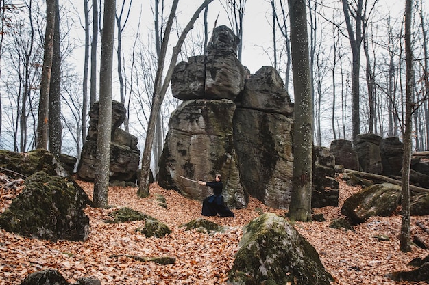 Homme en kimono noir pratiquant les arts martiaux avec une épée sur les rochers et fond de forêt