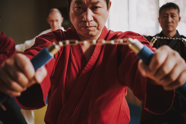 Photo homme en kimono rouge tenant un nunchuck dans ses mains.