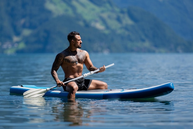 Photo homme sur le lac des alpes d'été homme musclé fort sexy pagayant sur une planche à pagaie ou sup vacances d'été en suisse style de vie d'été sport nautique d'été garçon fort nagant avec une planque à pagaie