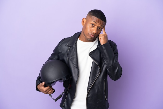 Homme latin avec un casque de moto isolé sur violet pensant une idée