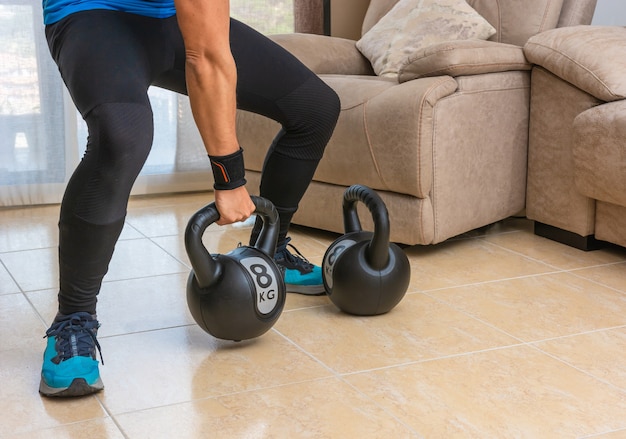 Homme latin effectuant un entraînement croisé à la maison avec une paire de kettlebells.