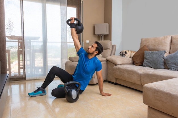 Homme latin effectuant un entraînement croisé à la maison avec une paire de kettlebells.