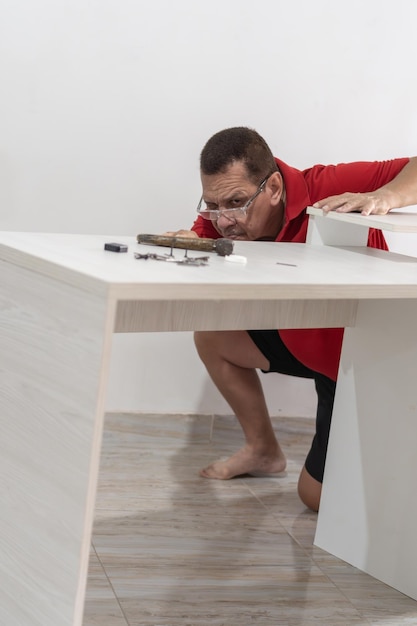L'homme latin en rouge assemblant des meubles concentré sur les détails