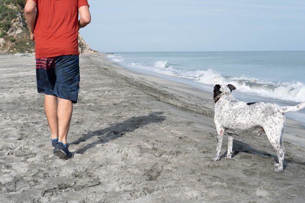 Homme latin s'amusant avec son chien sur la plage le matin