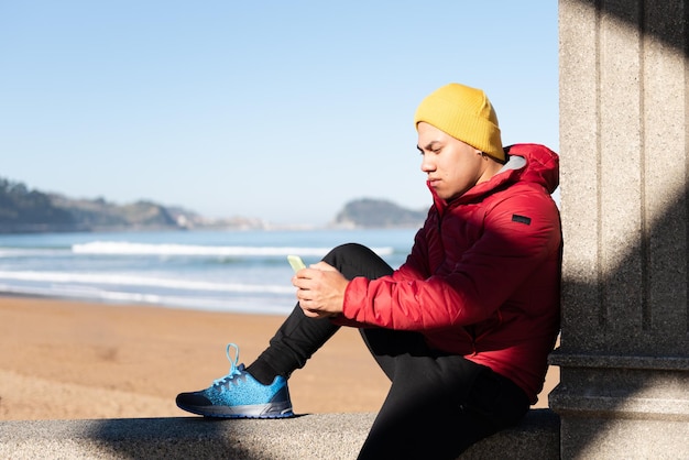 L'homme latin s'est concentré sur son téléphone alors qu'il était assis au bord de la mer. Concept de dépendance numérique.