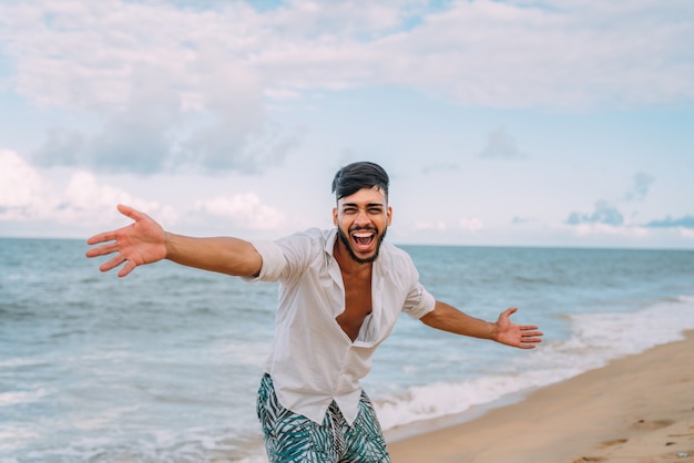 Homme latino-américain souriant et jetant son chapeau en regardant la caméra sur la plage par une belle journée d'été