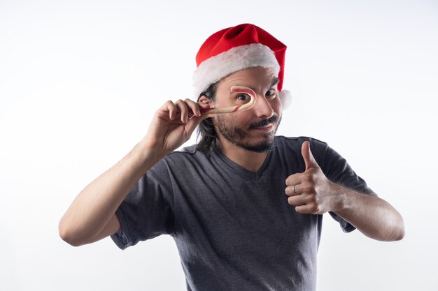 Photo homme latino avec chapeau de noël avec une canne en bonbon.