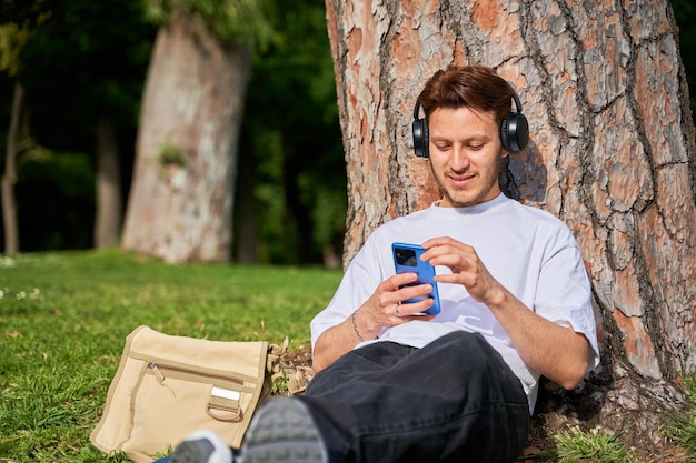 Un homme latino est assis sur l'herbe dans un parc appuyé contre un arbre