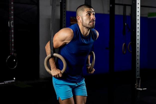 Un homme latino en vêtements de sport faisant des exercices de gymnastique sur certains anneaux dans une salle de sport