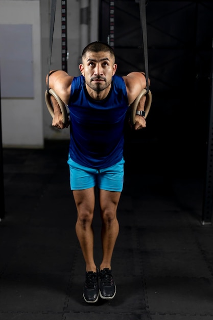 Un homme latino en vêtements de sport faisant des exercices de gymnastique sur certains anneaux dans une salle de sport