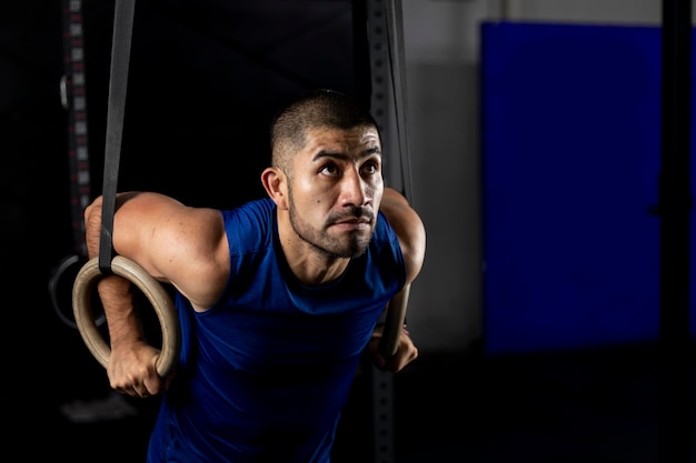 Un homme latino en vêtements de sport faisant des exercices de gymnastique sur certains anneaux dans une salle de sport