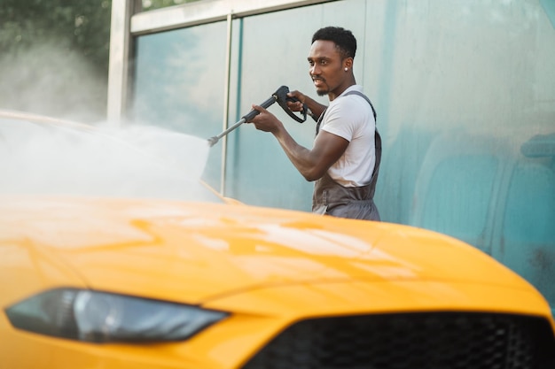 Homme lavant sa voiture jaune de luxe sous jet d'eau à haute pression à l'extérieur à la station de lavage de voiture