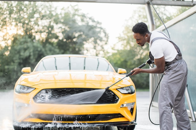 Homme lavant sa voiture jaune de luxe sous jet d'eau à haute pression