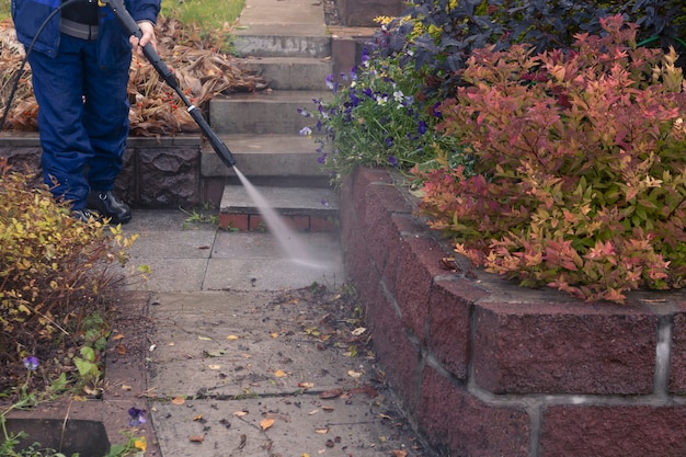 Un homme lave une allée de jardin avec un nettoyeur haute pression. Travaux d'automne dans le jardin.