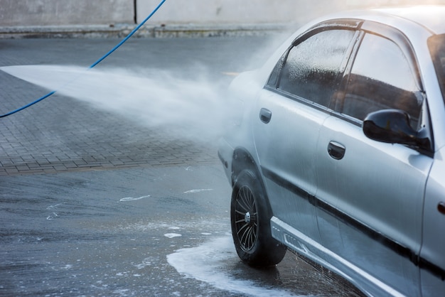 Un homme lave le détergent d'une voiture avec un jet d'eau dans un lave-auto en libre-service, gros plan