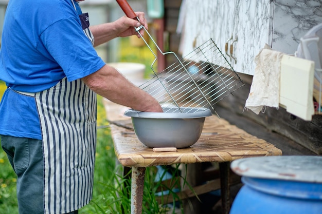 Un homme lave la grille du gril dans une bassine d'eau Nettoyage du gril pour faire frire la viande