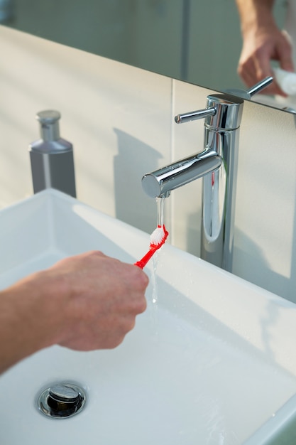 Homme lave sa brosse à dents sous l'évier dans la salle de bain