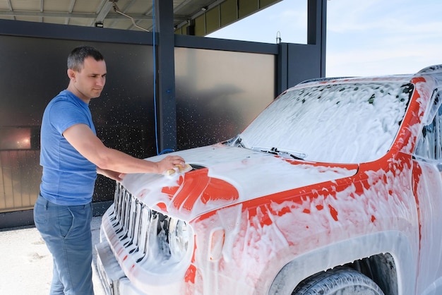 Un homme lave sa voiture avec une éponge dans un lave-auto Voiture en mousse