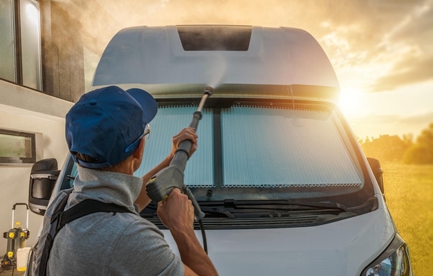 Un homme lave son camping-car sous pression pendant un coucher de soleil pittoresque