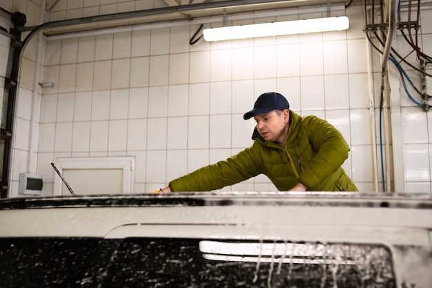L'homme lave la voiture après avoir lavé la carrosserie en essuyant la surface de la voiture avec un gant de nettoyage spécial