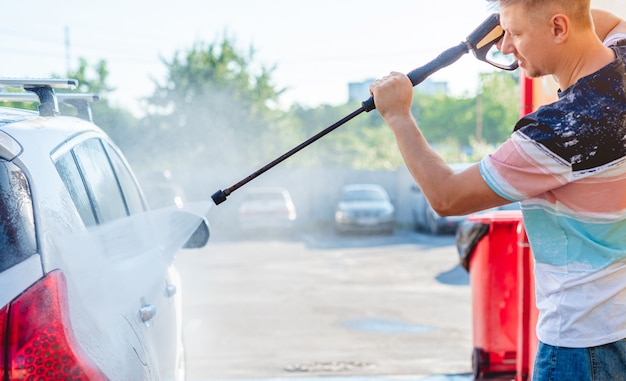 L'homme lave la voiture avec de l'eau à haute pression