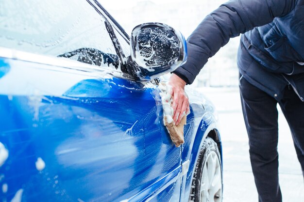 Un homme lave la voiture avec un gant de toilette. lave-auto en libre-service