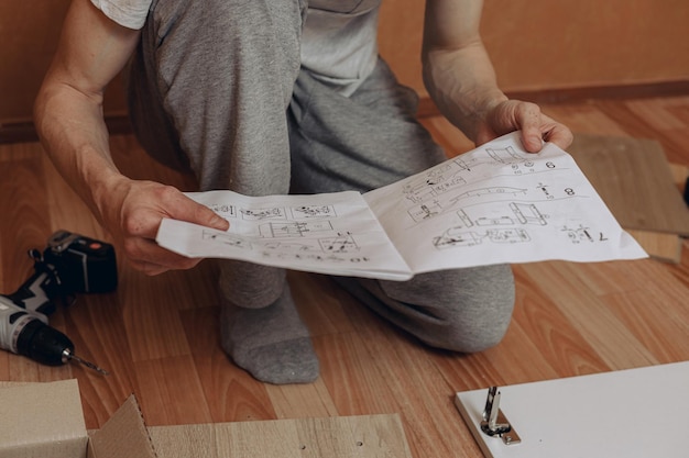 homme lisant des instructions et assemblant des meubles assis sur le sol avec des détails en bois