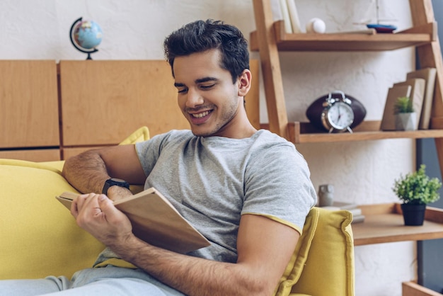 Homme lisant un livre et souriant sur un canapé dans le salon