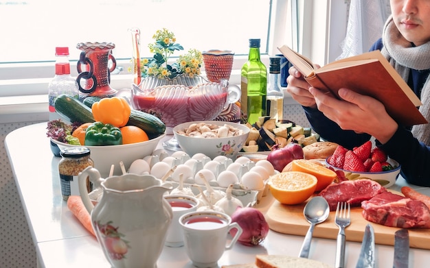 Homme lisant un livre sur une table à manger avec divers ingrédients de cuisine pour la célébration du festival en hiver