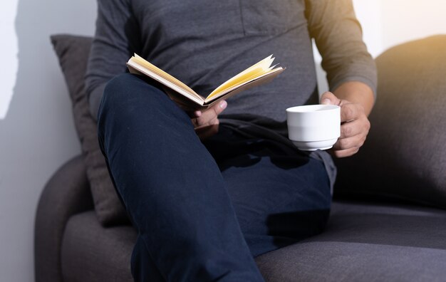 homme lisant un livre et tenant une tasse de café