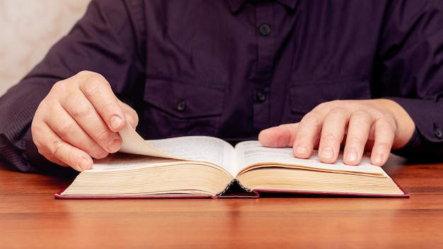 Un homme lit la Bible assis à une table. Un livre ouvert entre les mains d'un homme