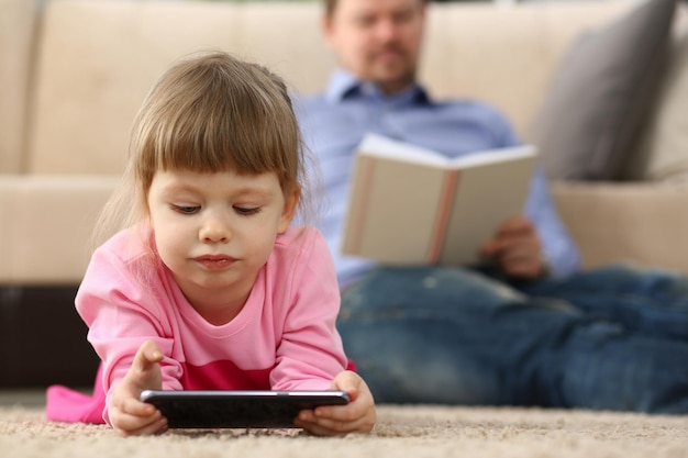 L'homme lit un livre enfant joue avec un smartphone à la maison