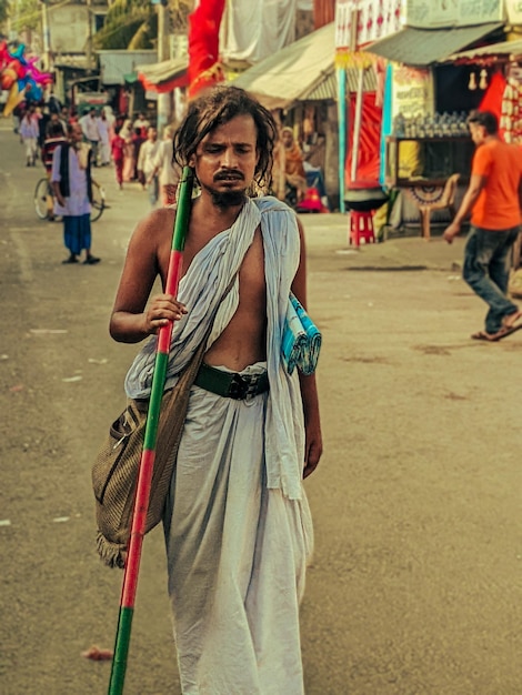 Photo un homme avec un long bâton marche dans la rue avec un poteau rouge et vert.