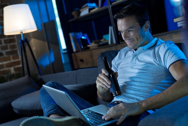 Photo homme lumineux insouciant positif passer une bonne soirée à la maison tout en buvant de la bière