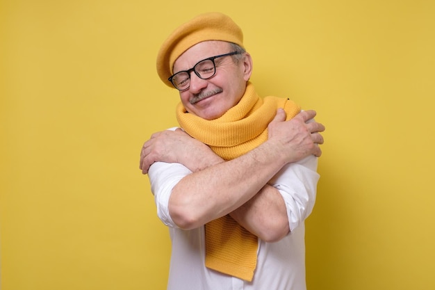 L'homme à lunettes et chapeau et écharpe jaunes se serre dans ses bras a une haute estime de soi