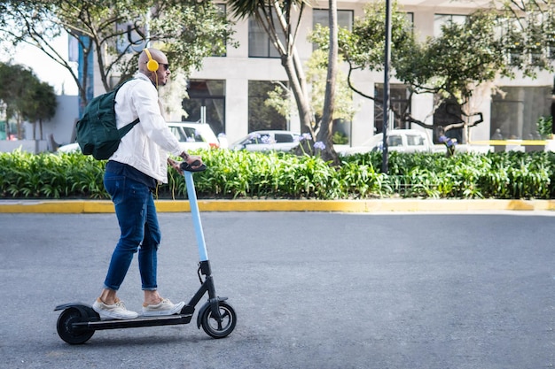 Homme avec des lunettes et des écouteurs sur un scooter électrique dans une rue de la ville