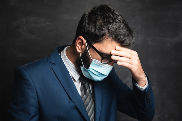 Un homme avec des lunettes et un masque regarde pensivement sur une surface sombre