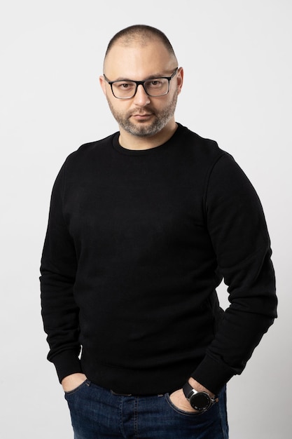 Un homme avec des lunettes à monture noire et un pull noir garde ses mains dans ses poches