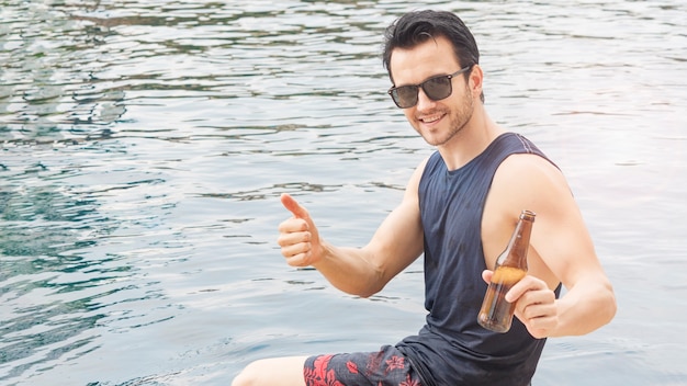 Homme de lunettes noires avec boisson de bouteille de bière à la piscine