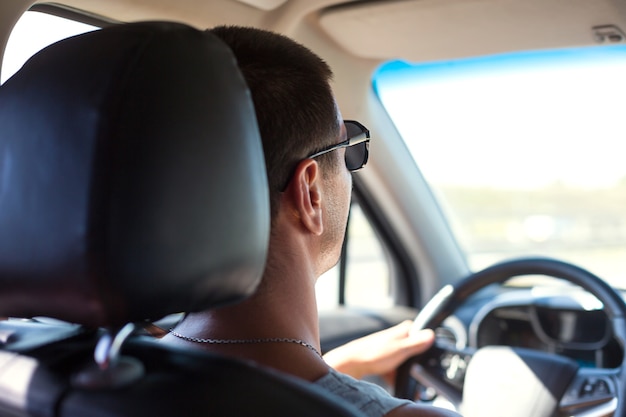 Un homme avec des lunettes noires conduit une voiture. Sécurité routière, règles de circulation, déplacements en voiture, navigateur