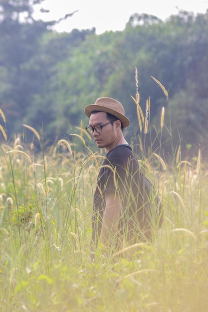 Un homme avec des lunettes pose parmi l'herbe et l'herbe avec un chapeau de cowboy