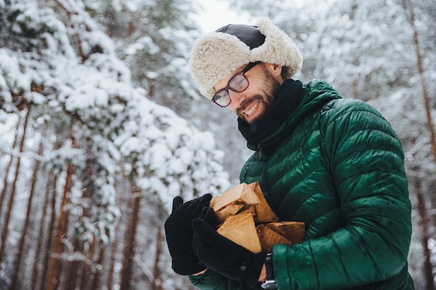 Homme à lunettes regarde avec bonheur le bois de chauffage dont il se connecte dans la forêt d'hiver